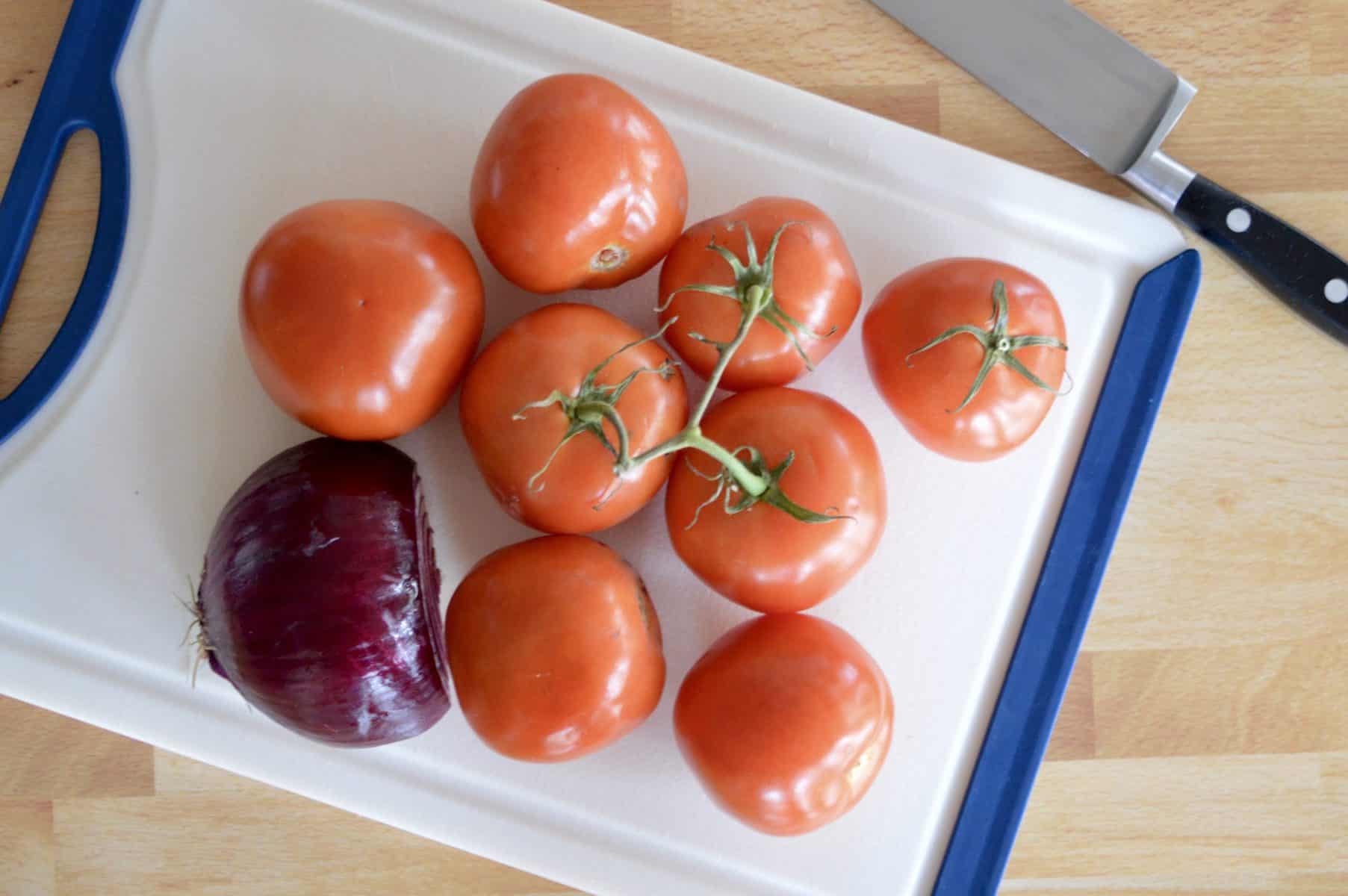 fresh tomatoes and red onion on a white cutting board. 