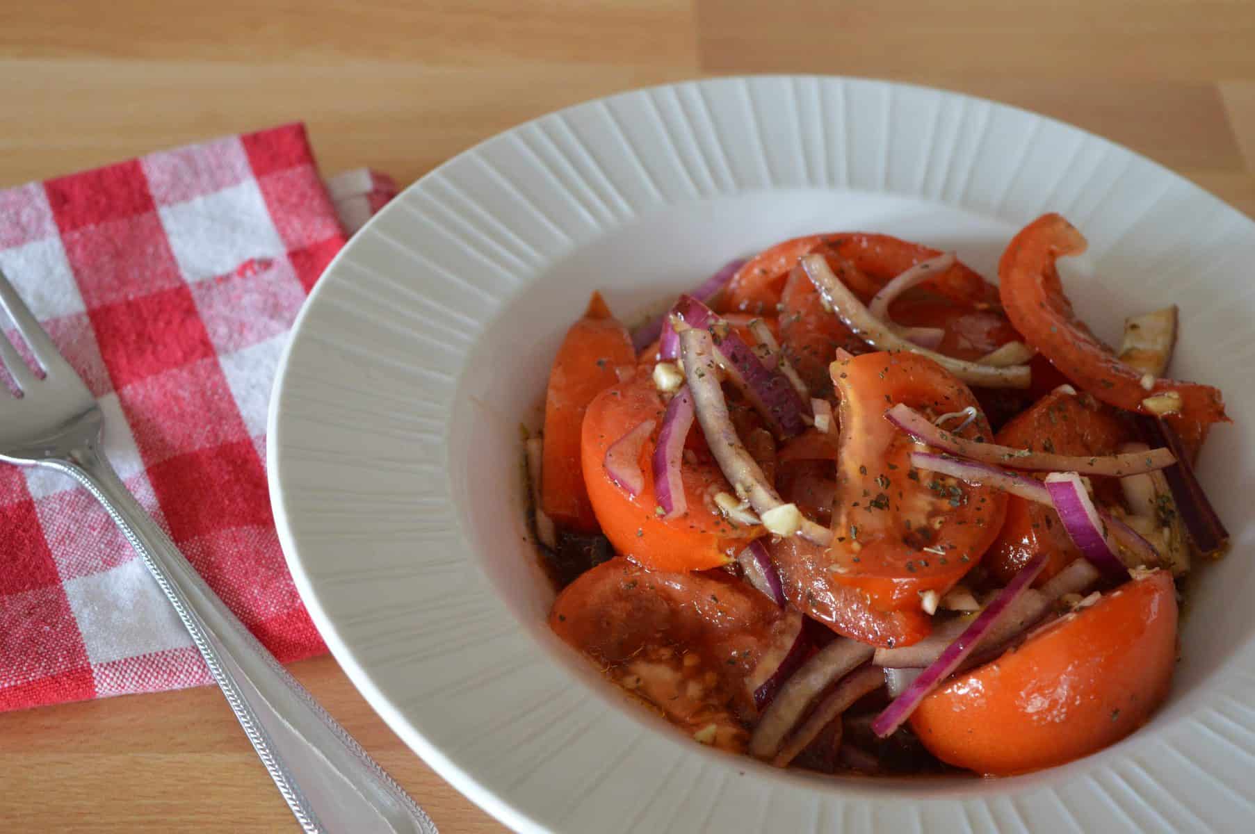 Italian Tomato Onion Salad in a white bowl with a red and white checker napkin next to it. 