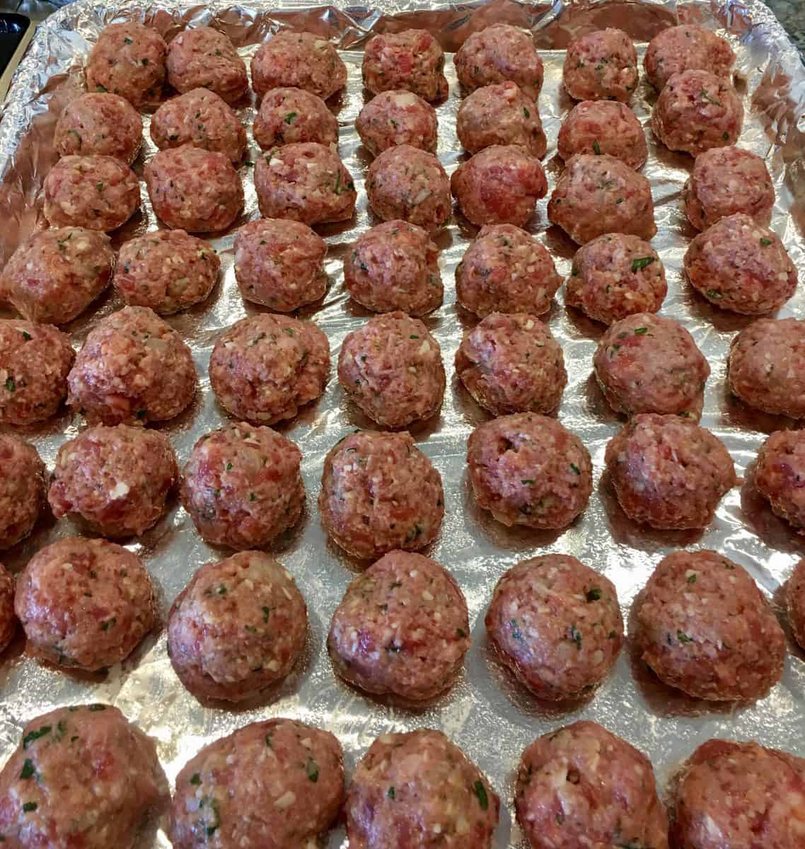 balls of meat rolled on a foil lined baking sheet.