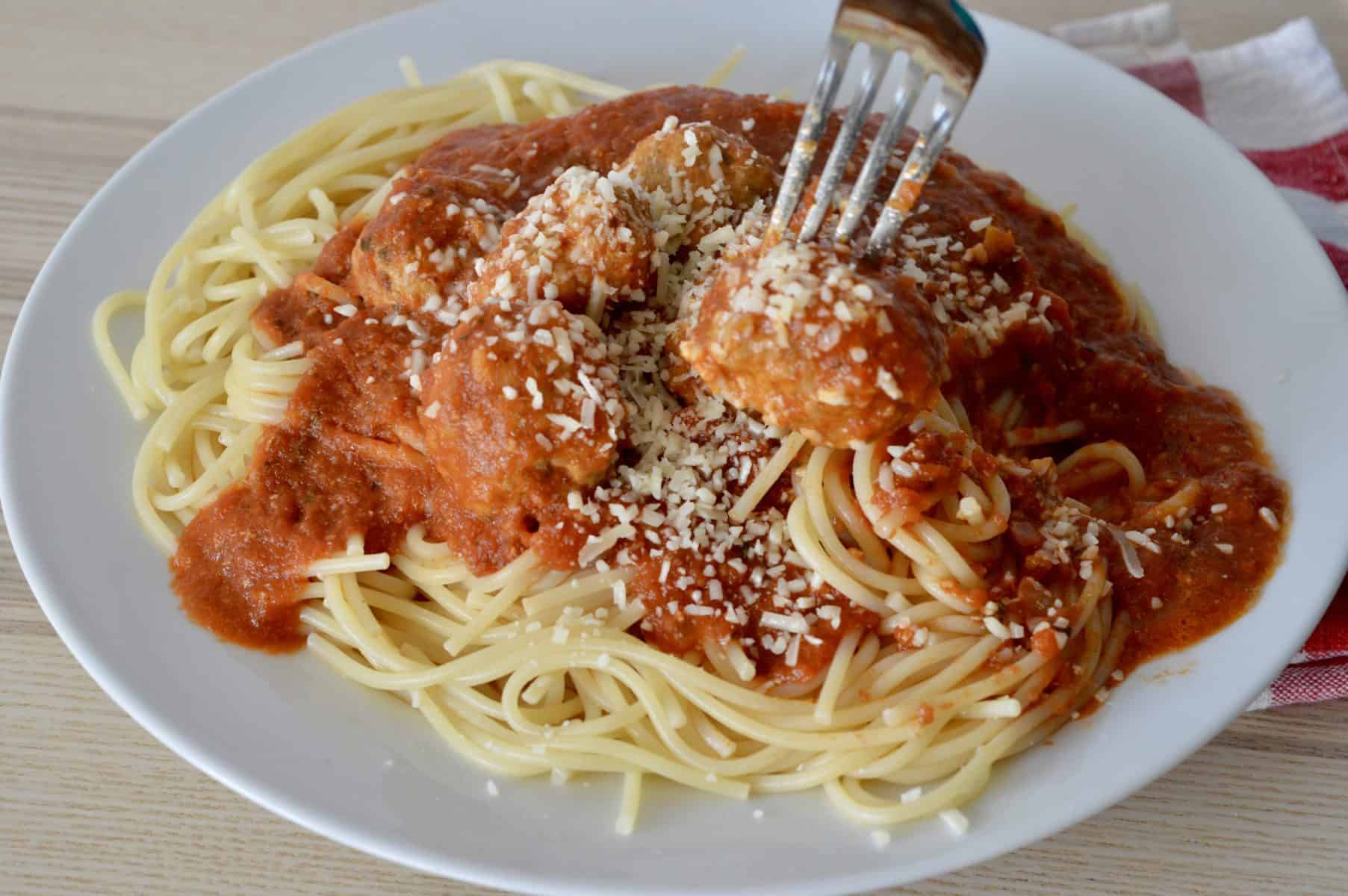 Italian Turkey Sausage Meatballs in marinara sauce over spaghetti in a white plate. 