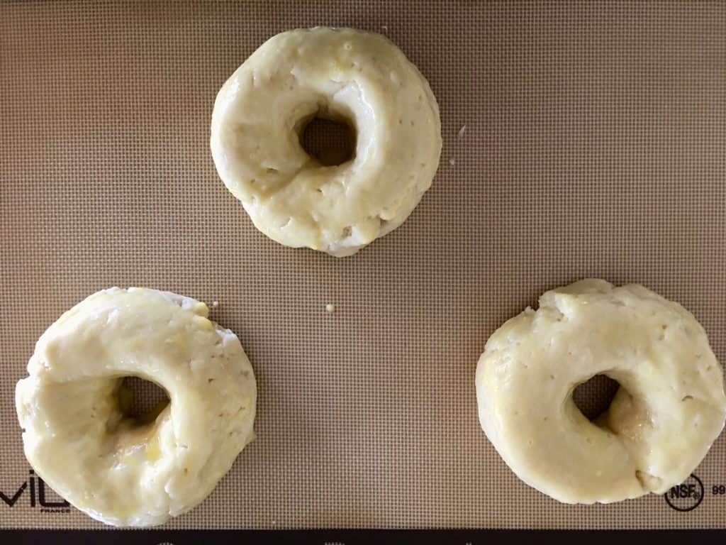 dough formed into donut shapes on a baking mat.