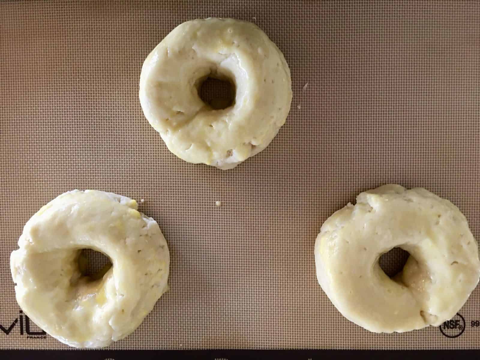 dough formed into donut shapes on a baking mat. 