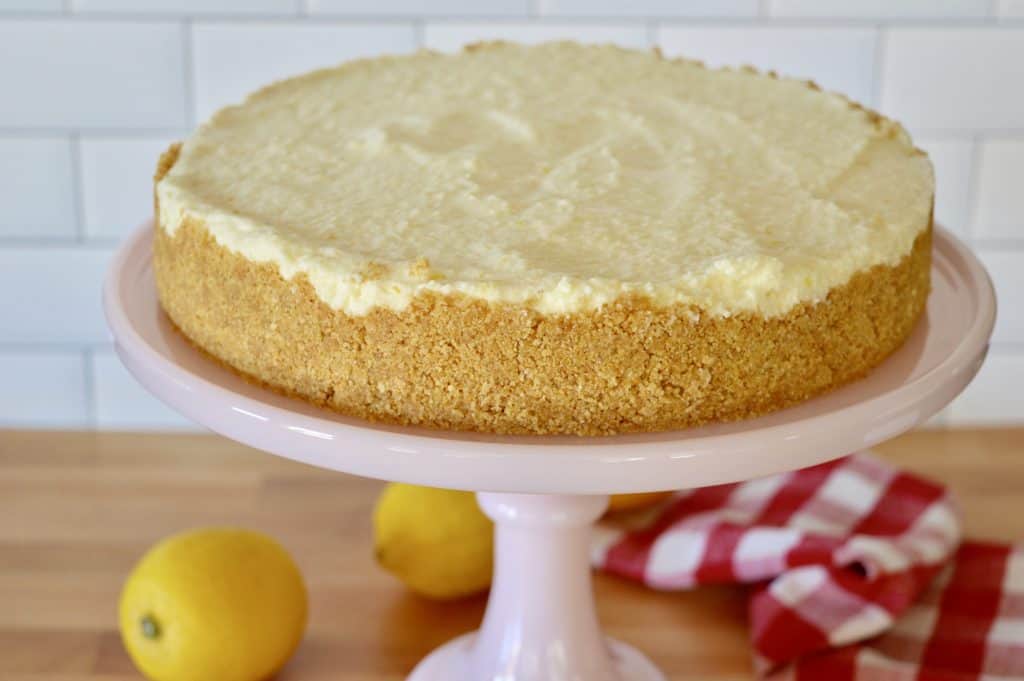 ungarnished no-bake lemon mascarpone cheesecake on a pink cake pedestal.