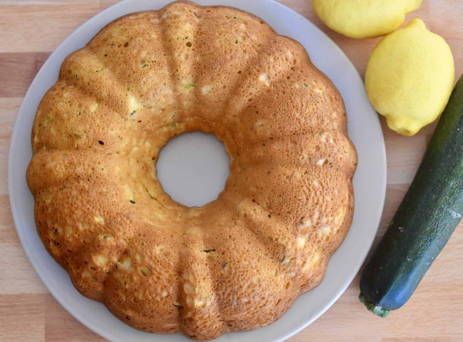 overhead photo of zucchini ricotta bundt cake with a zucchini and lemons next to it. 