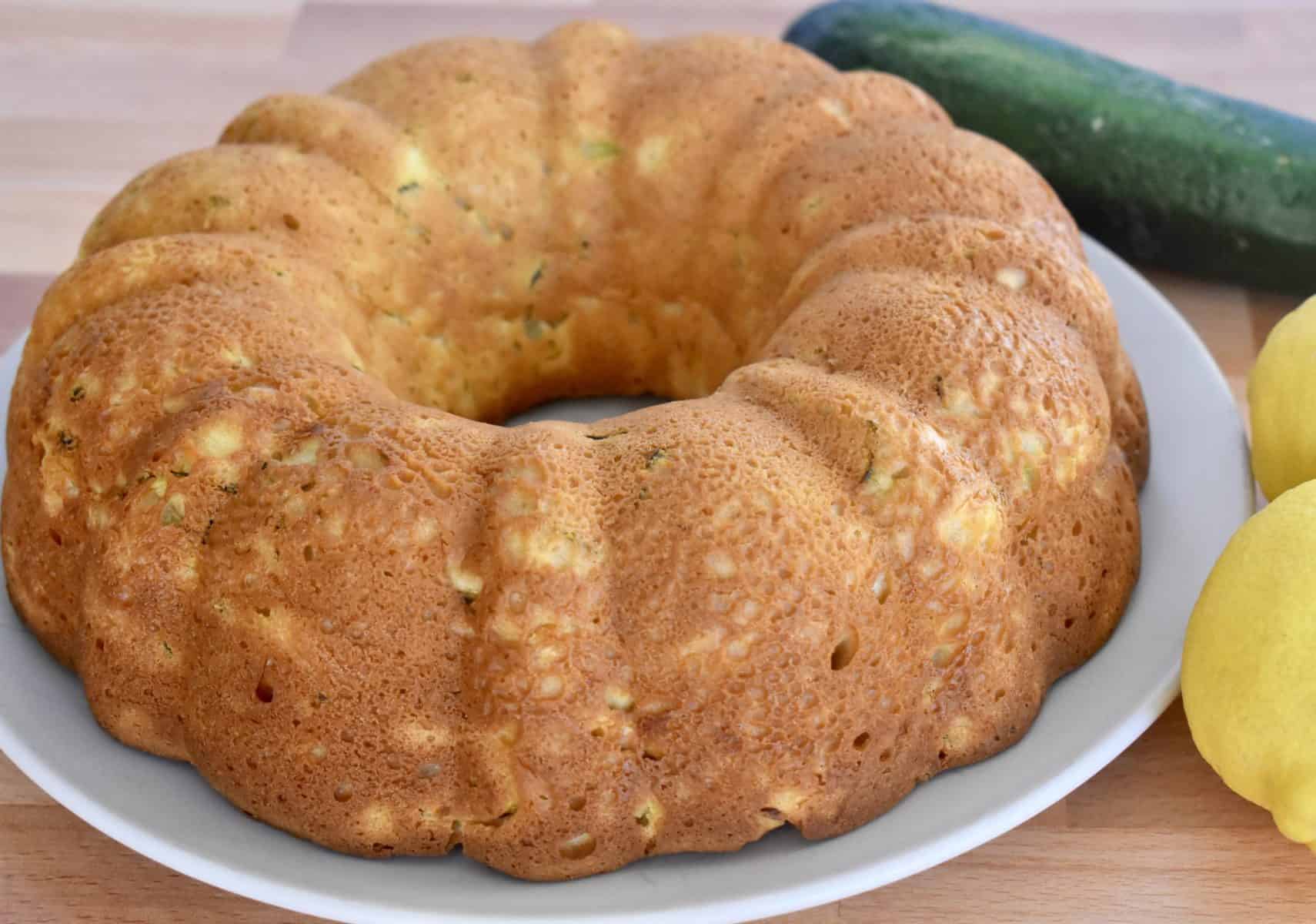 Zucchini Ricotta Cake on a plate with lemon and zucchini next to it. 