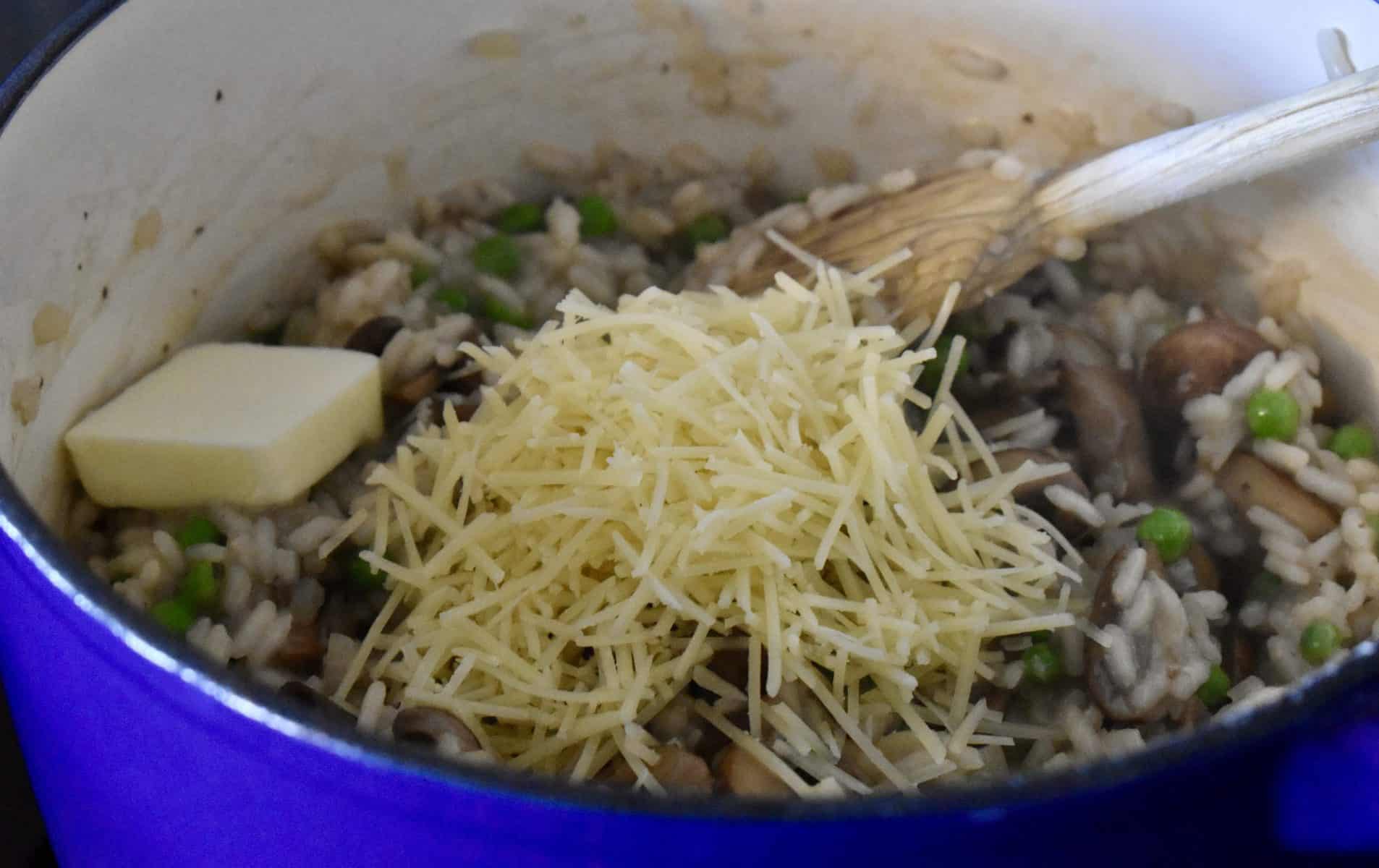 butter and parmesan cheese on the mushroom pea risotto in the pot.
