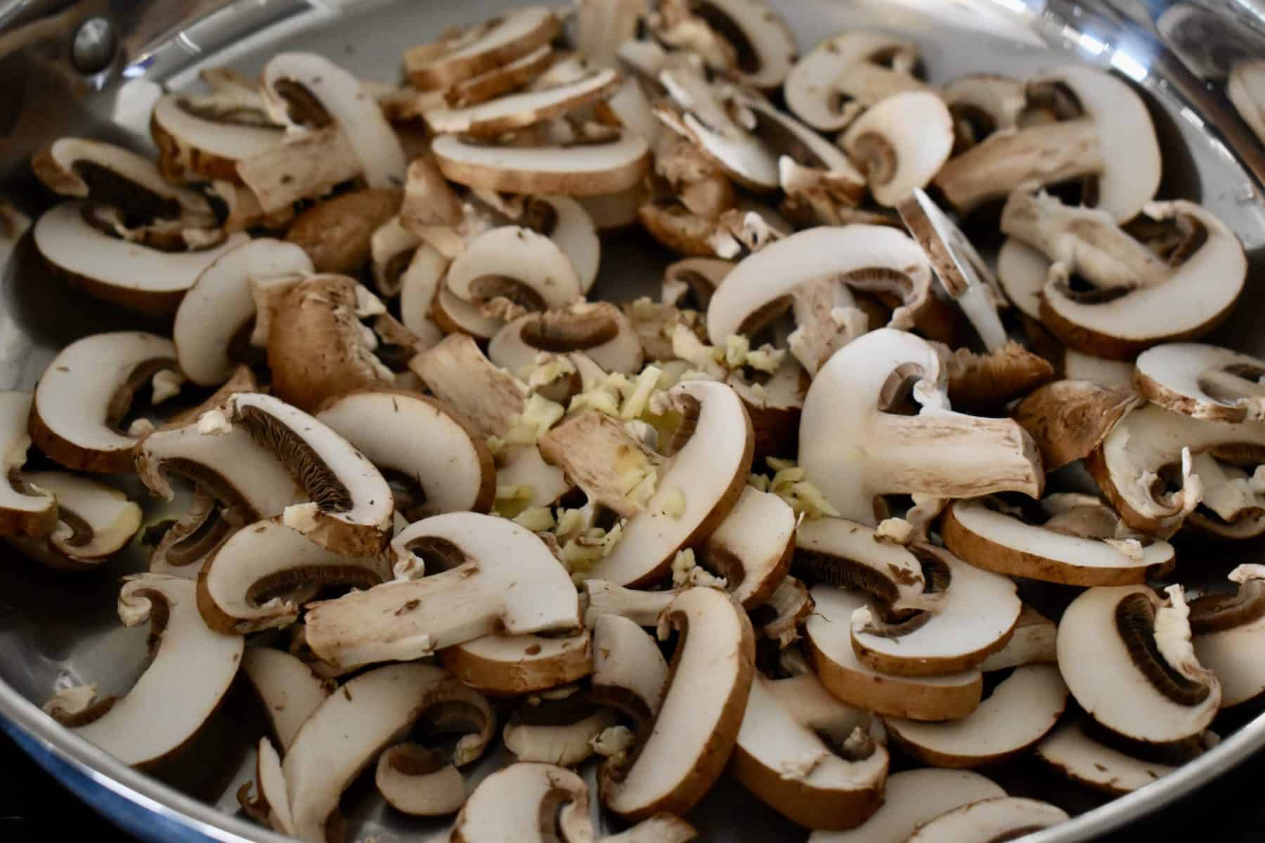 Mushrooms in a large pan with garlic on top.