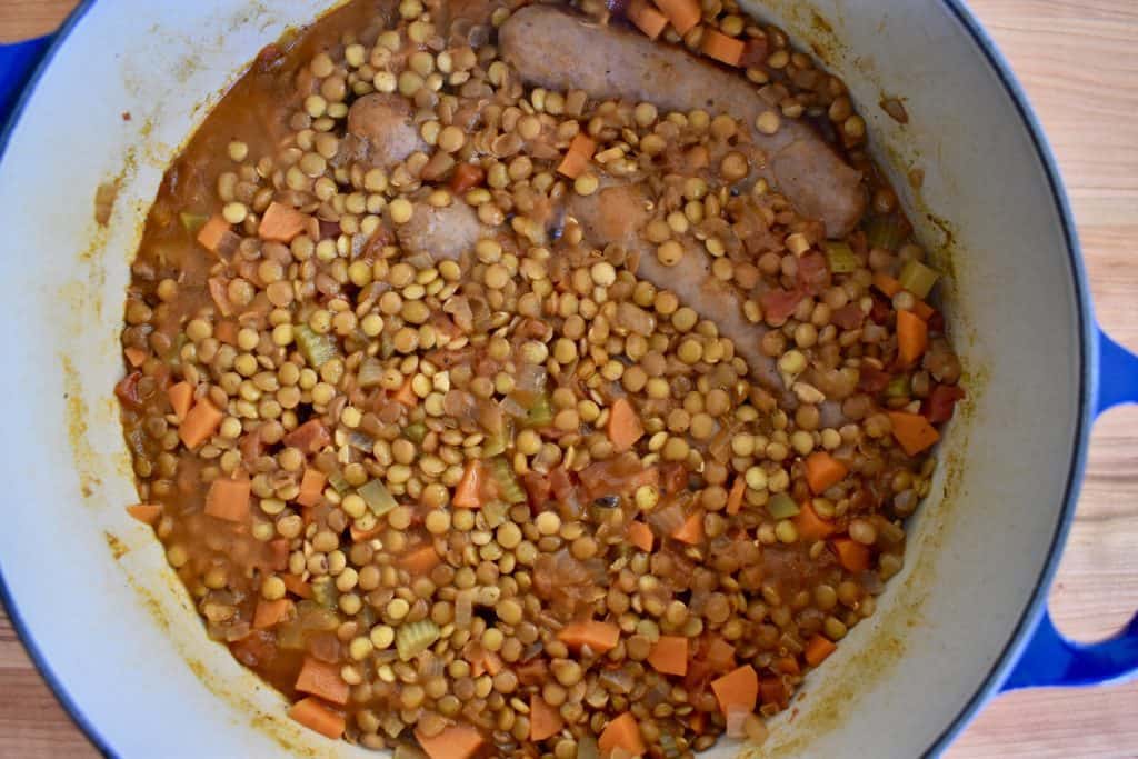 Cooked lentils and sausage in a blue dutch oven pot.