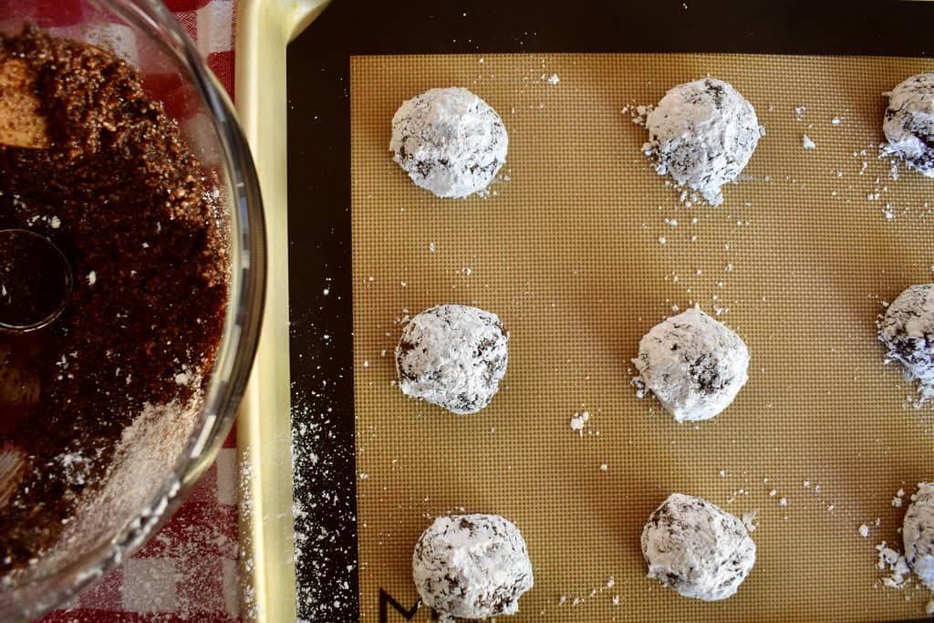 Cookies rolled in powdered sugar on lined baking sheet.