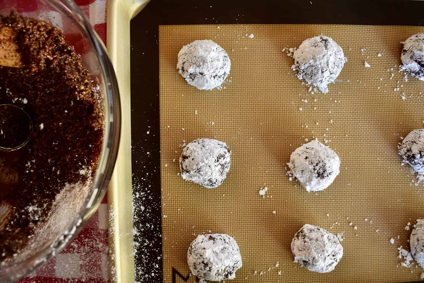 Cookies rolled in powdered sugar on lined baking sheet. 