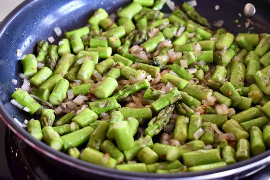 cooked asparagus and shallots in a pan.