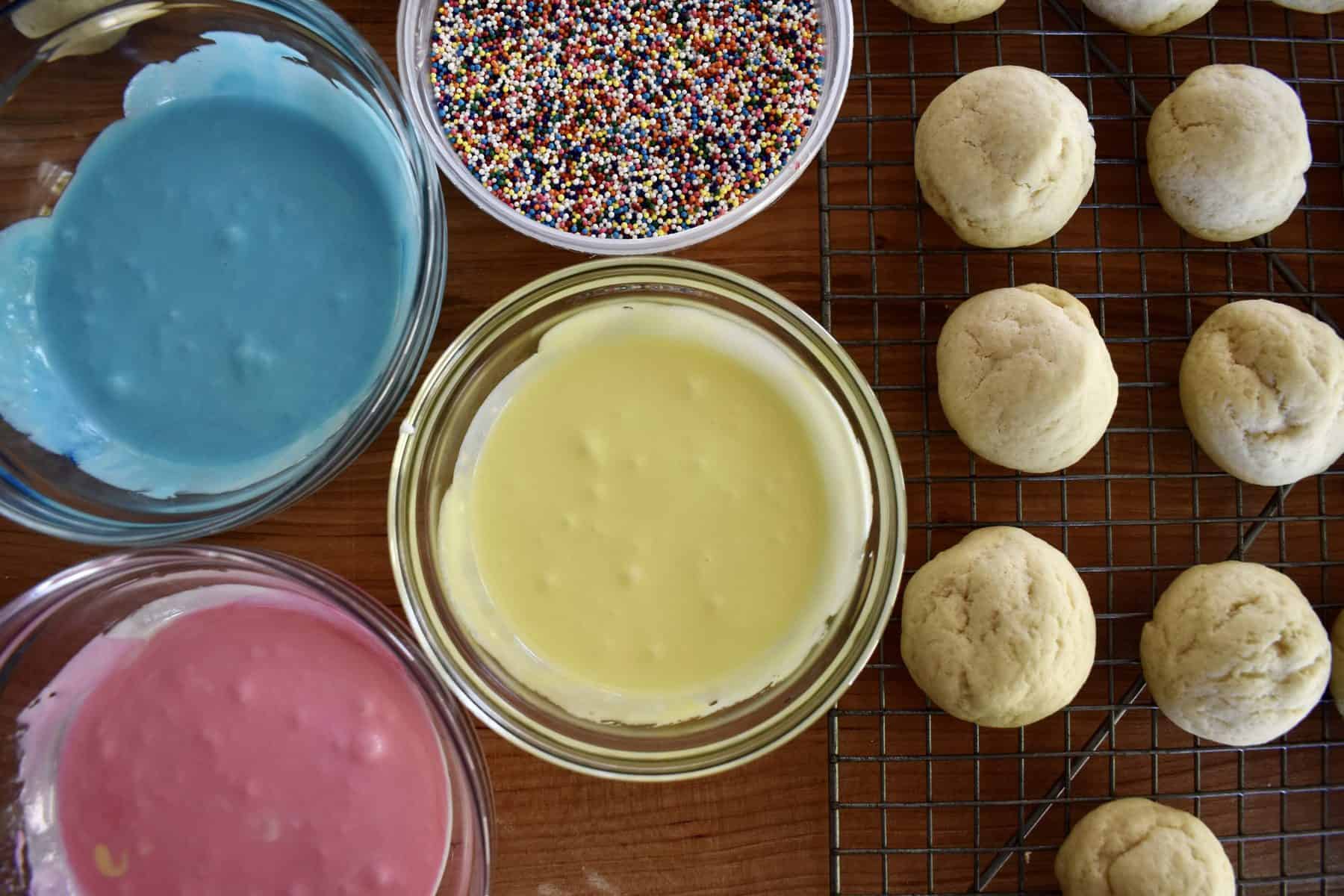 overhead of frosting, sprinkles, and cookies on a wire cooling rack 