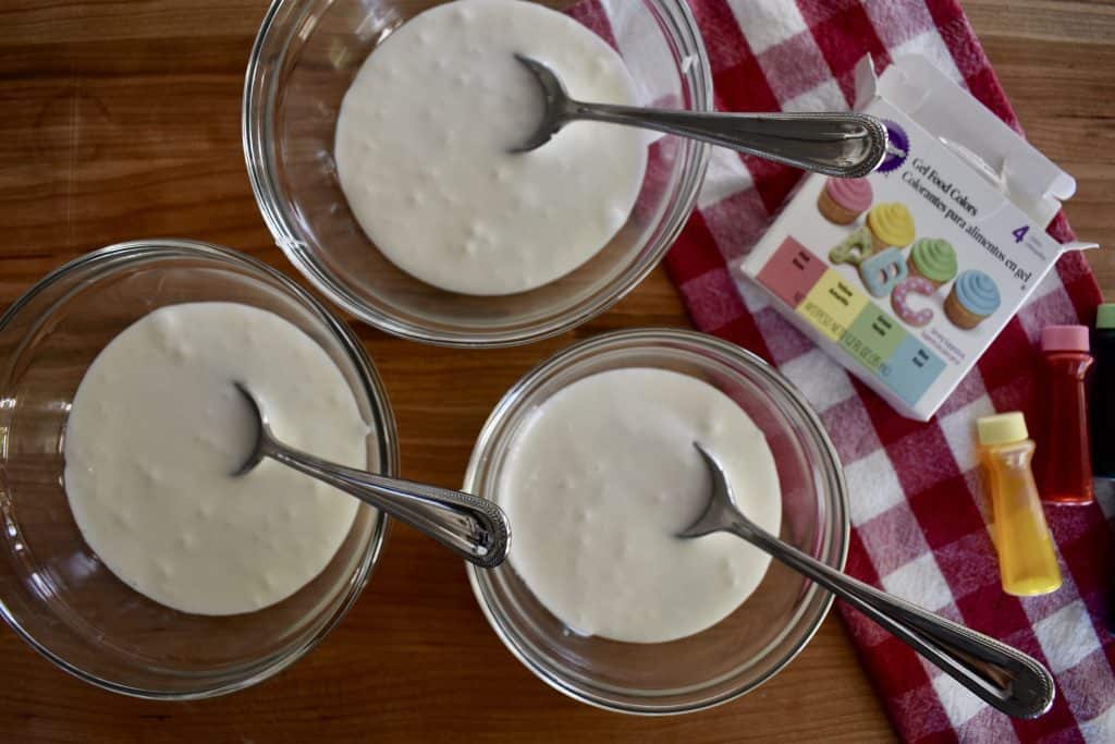 three bowls of white frosting with spoons in them.