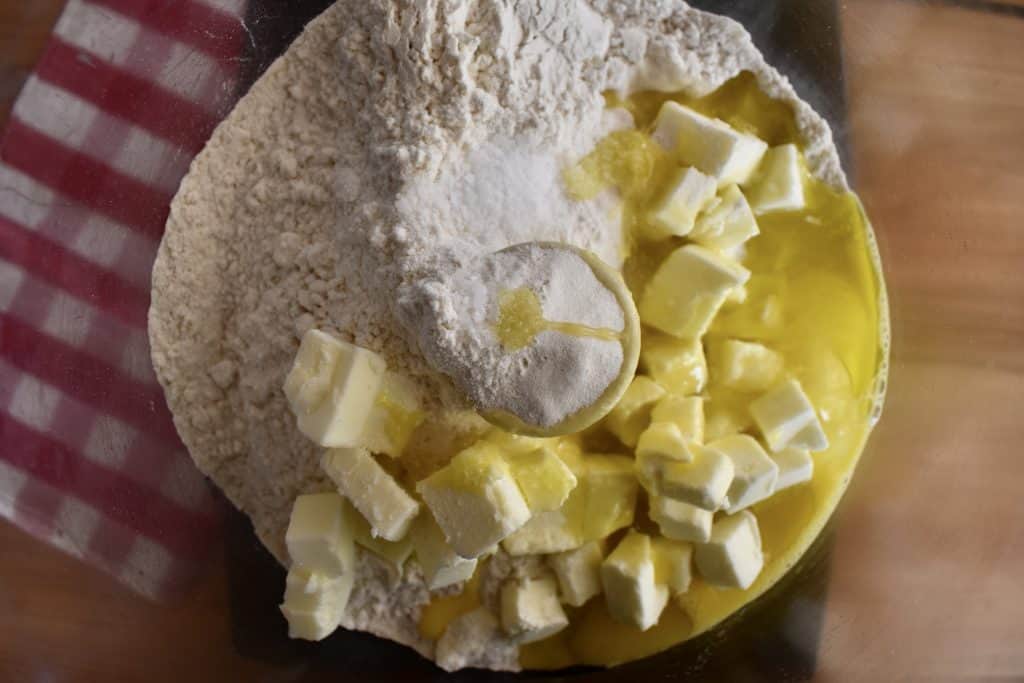 Food processor with flour, butter, olive oil, and egg.