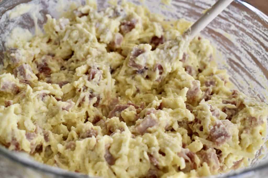 Ricotta and cured meats stirred together in a large mixing bowl.