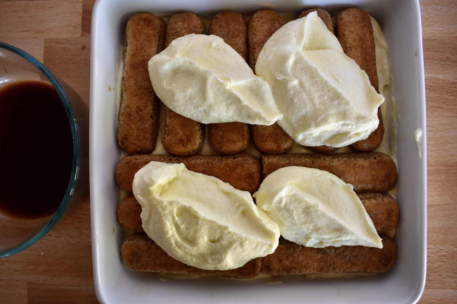 Scoops of mascarpone custard on the ladyfingers layer in a white dish. 