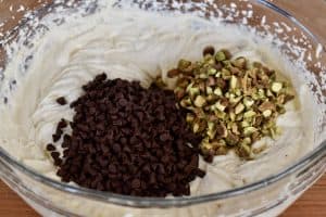 mini chocolate chips and diced pistachios added to the cream cheese ricotta mixture in a glass bowl.