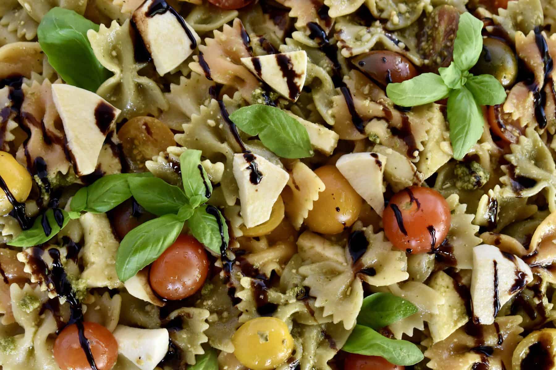 Overhead closeup photo of pesto pasta salad with balsamic drizzle overtop. 