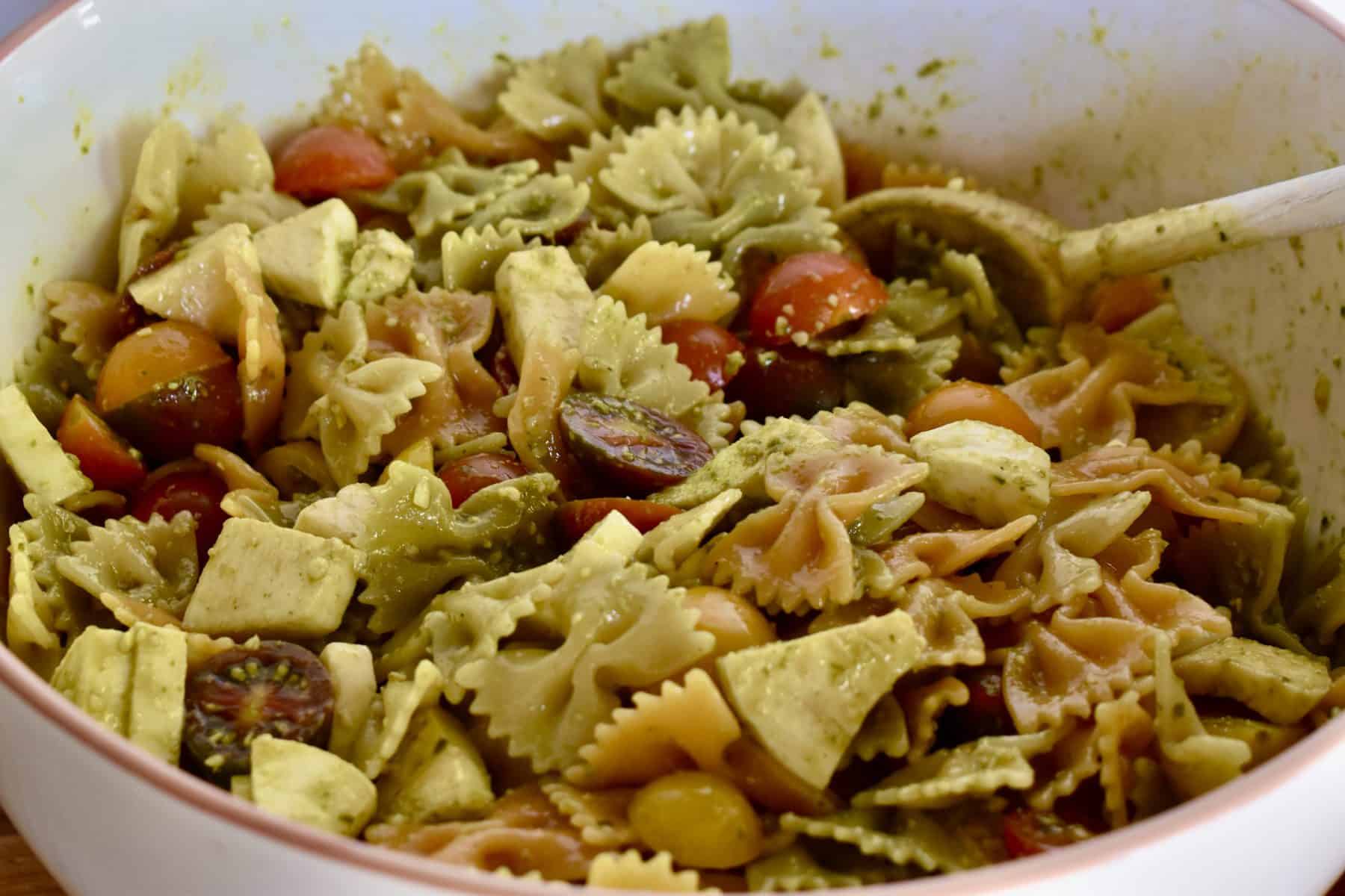 Pesto Pasta Salad tossed together in a large mixing bowl with a wooden spoon. 