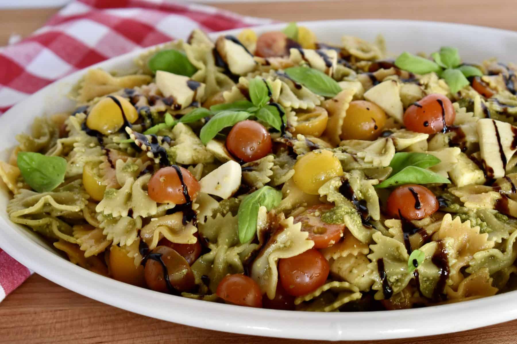 Recipe in a large white oval serving bowl with basil and drizzle overtop. 