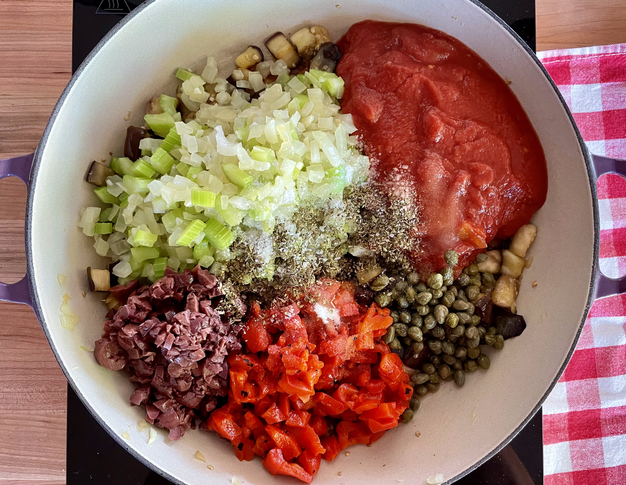 overhead photo of tomatoes, onion mixture, olives, capers, and diced bell peppers in a skillet. 