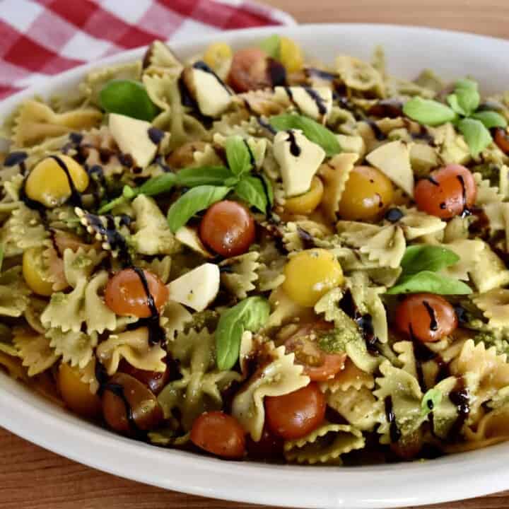 Pesto Pasta Salad in a large white oval platter garnished with basil and balsamic glaze.