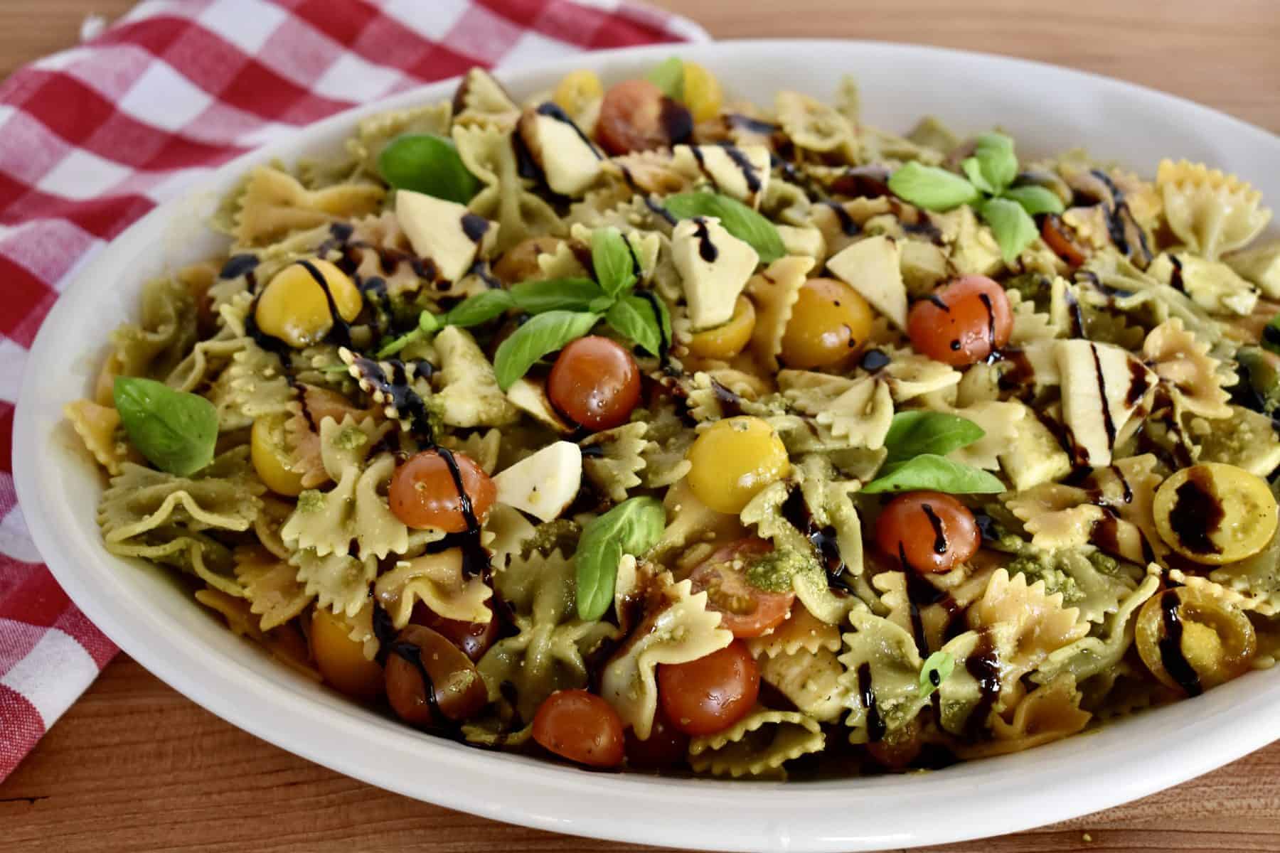 Pesto Pasta Salad in a large white oval platter garnished with basil and balsamic glaze. 