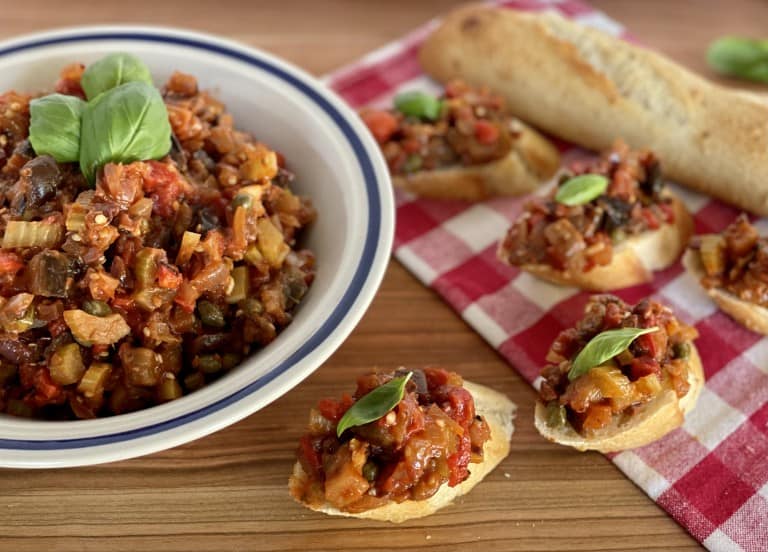 Eggplant Caponata on bruschetta on a wooden cutting boad.