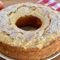 Italian Apple Cake on a wood cutting board with checkered cloth in the background.