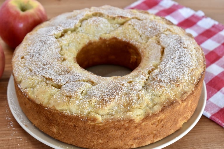 Italian Apple Cake on a wood cutting board with checkered cloth in the background.