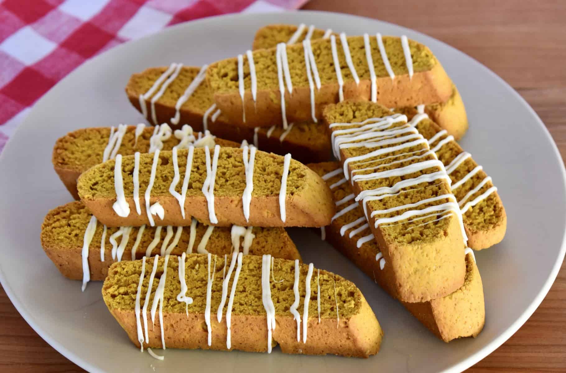 Pumpkin Biscotti with white chocolate drizzle stacked on a plate. 