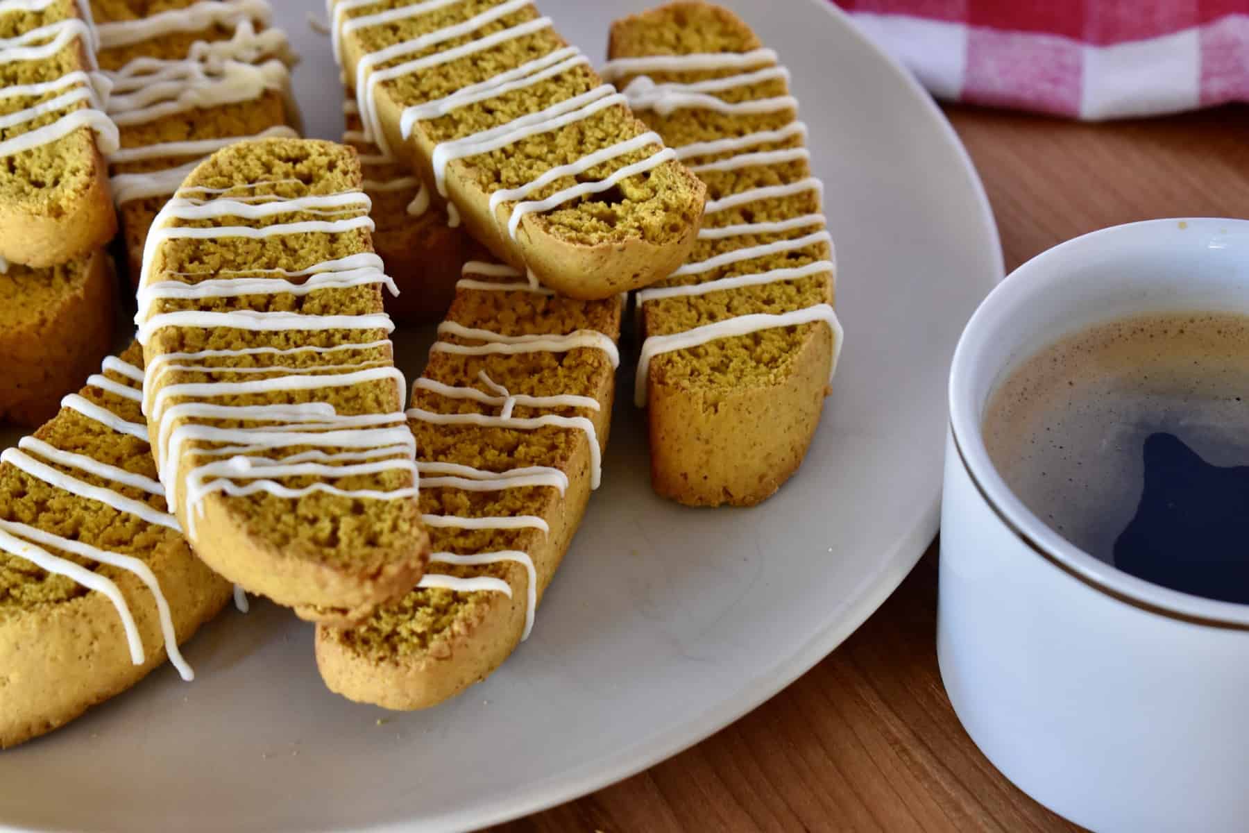 Pumpkin biscotti stacked on a plate with a cup of coffee next to it. 