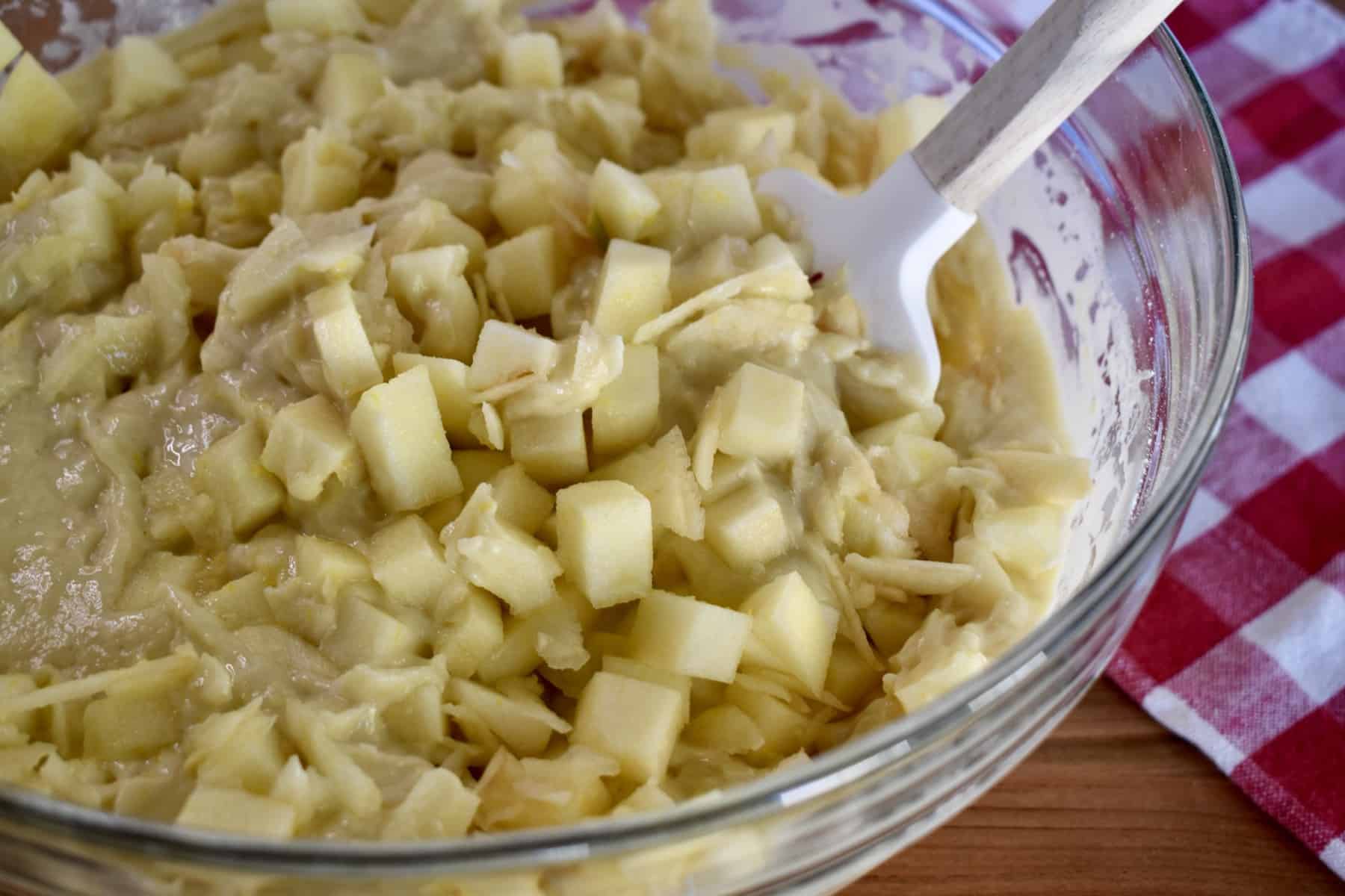 diced apples being folded into the cake batter with a rubber spatula. 