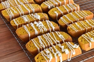 pumpkin biscotti on a wire cooling rack with white chocolate drizzled on them.
