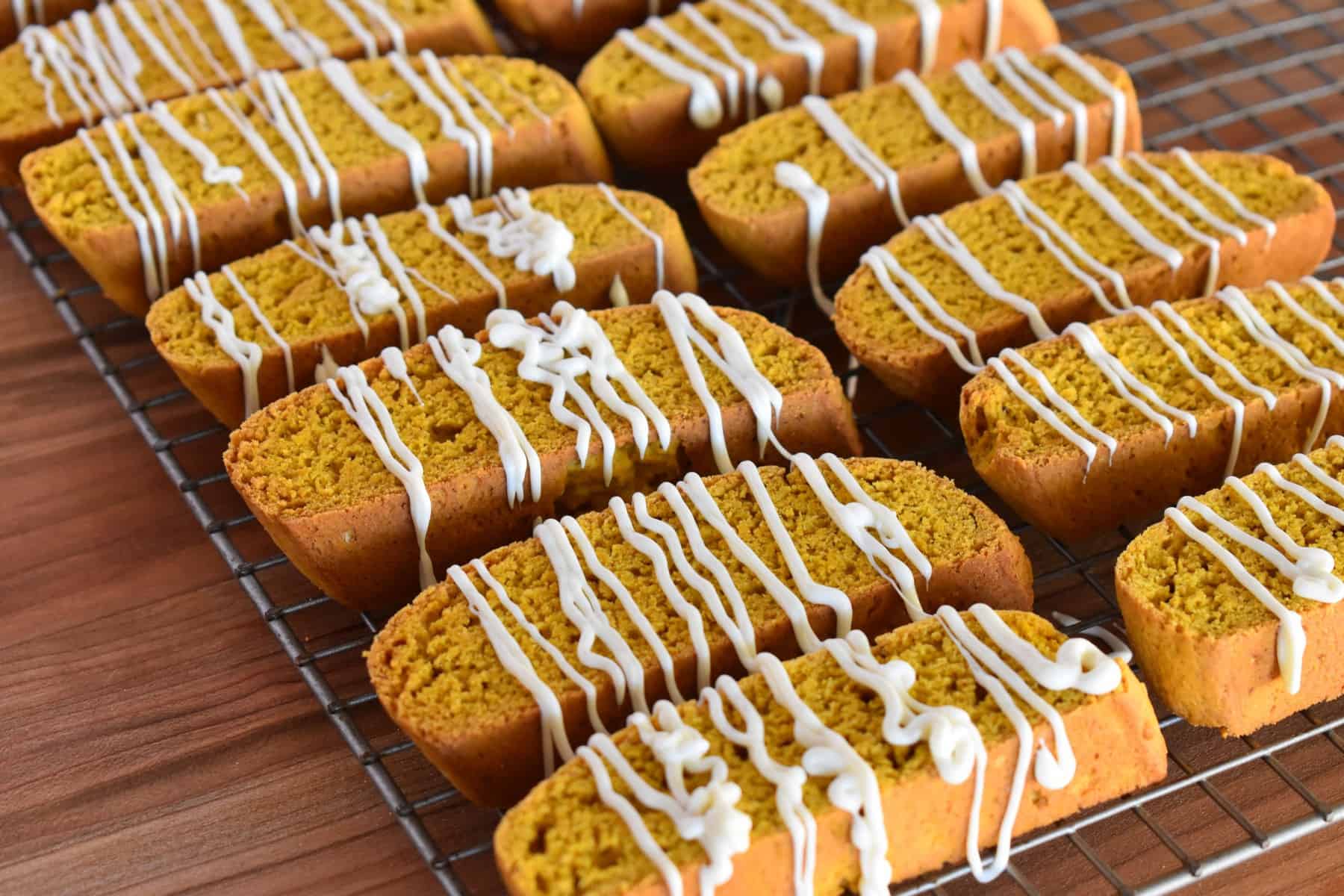 pumpkin biscotti on a wire cooling rack with white chocolate drizzled on them. 