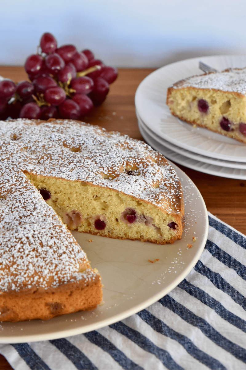 Italian grape cake on a white plate with a slice of the cake and a bunch of purple grapes. 