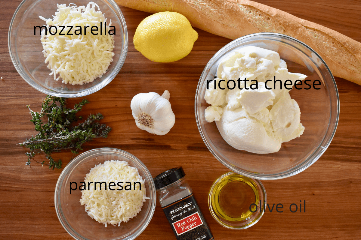 overhead photo of ingredients including thyme, lemon, cheeses, and olive oil. 
