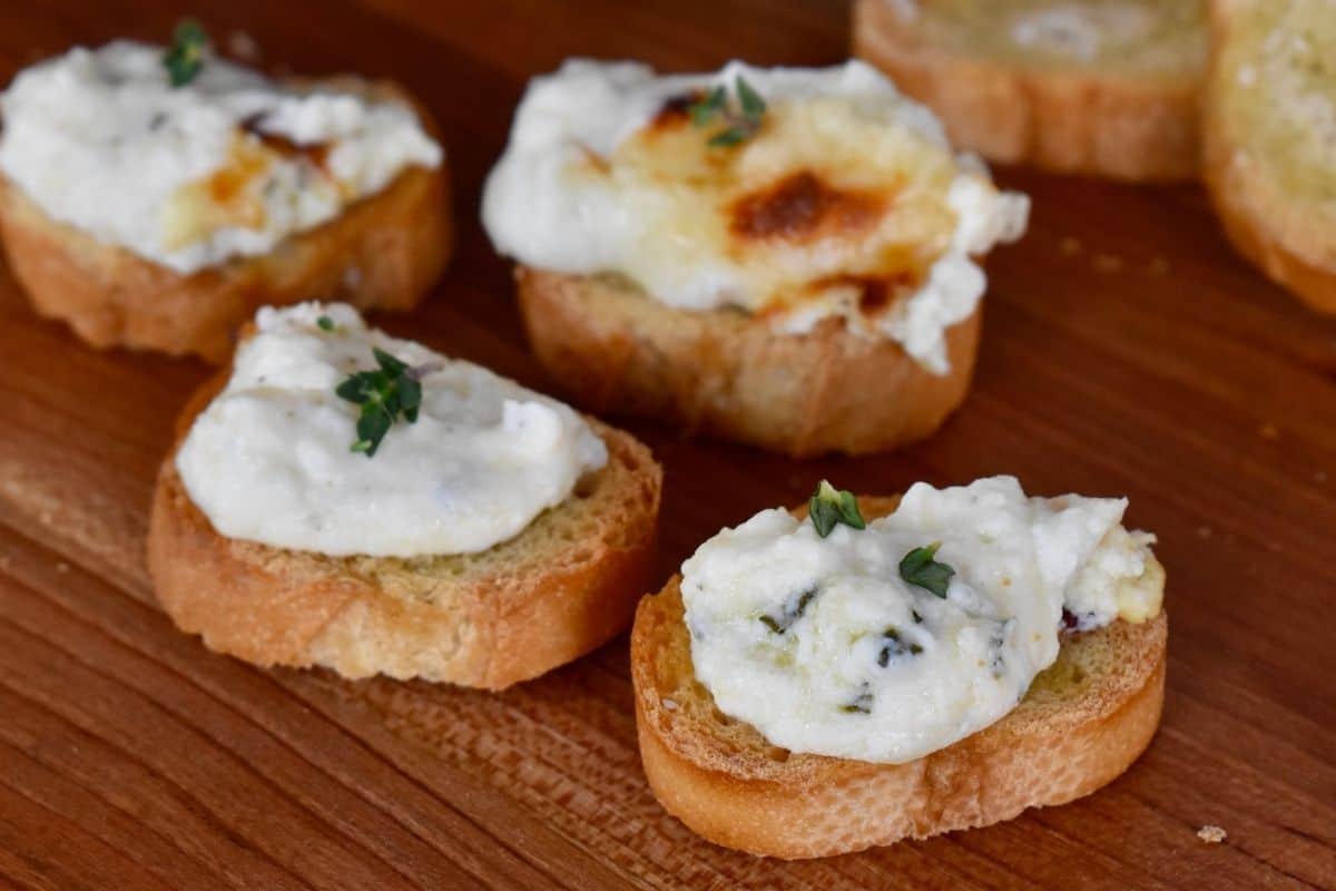 Baked Ricotta spread of slices of crostini on a wooden cutting board. 