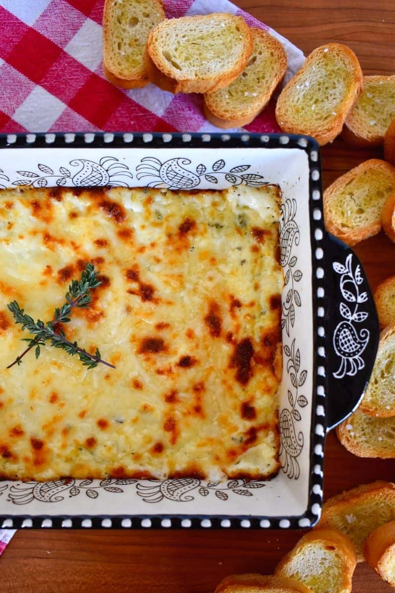 Baked Ricotta in a baking dish with crostini around it on a wooden cutting board. 