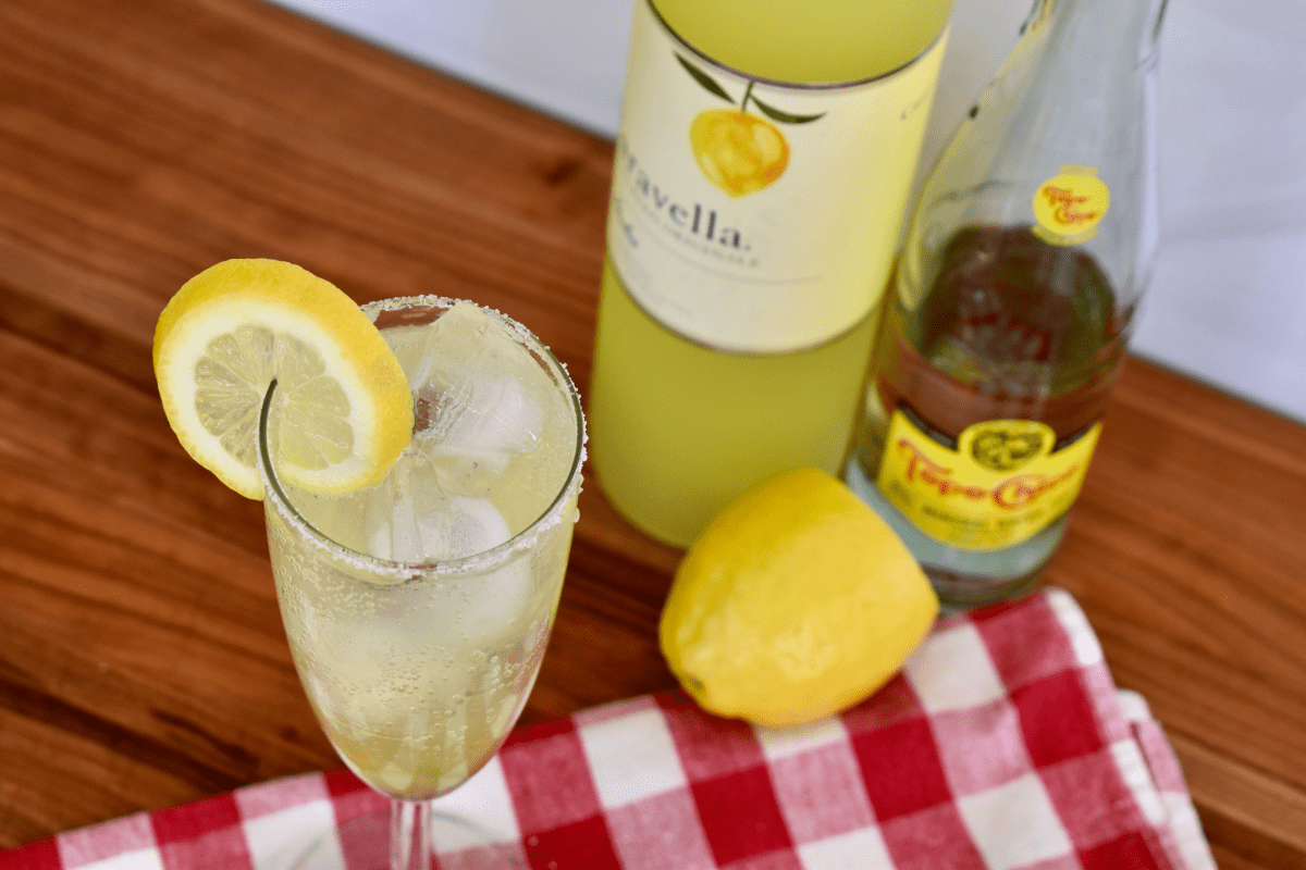 Limoncello Spritz on a counter with limoncello, lemon, and sparkling water behind it. 