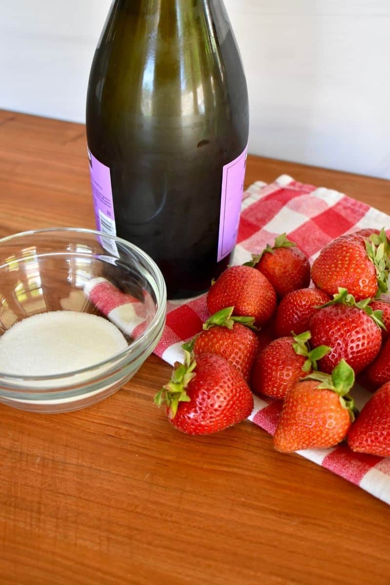 bottle of prosecco, strawberries, and sugar on a wood countertop. 