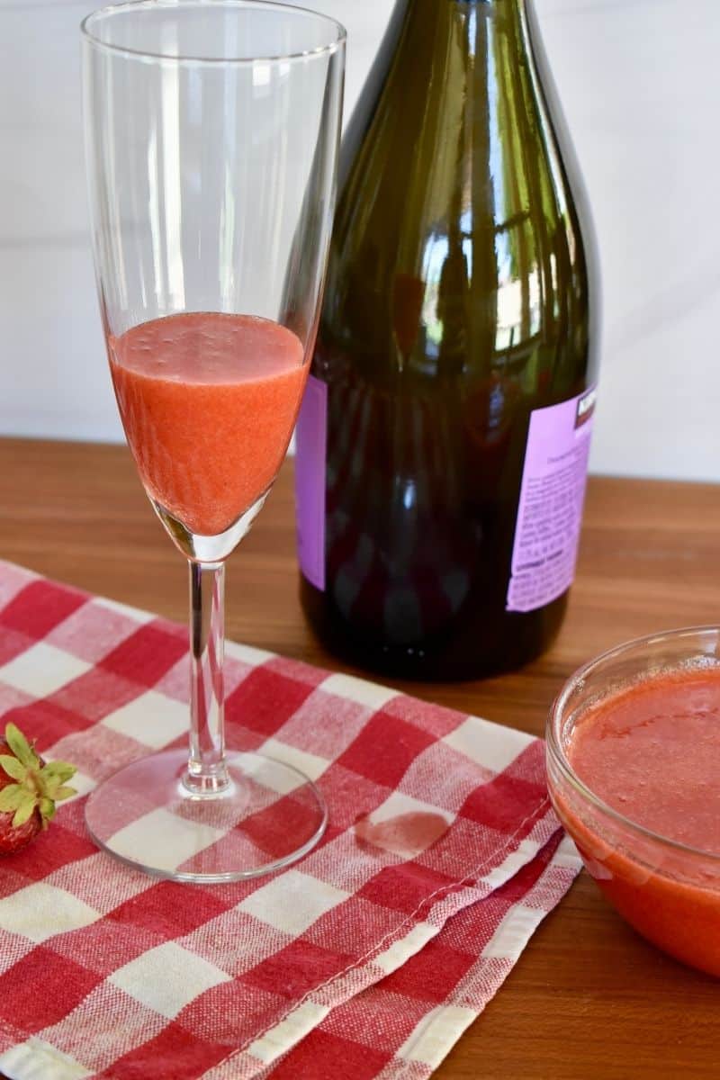 Strawberry puree in a champagne glass with a bottle of prosecco behind it. 