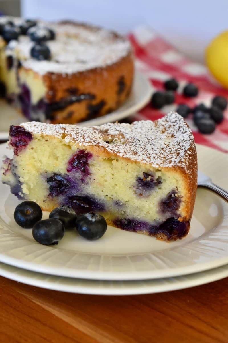 Blueberry Ricotta Cake on a plate with a lemon and cake in the background. 