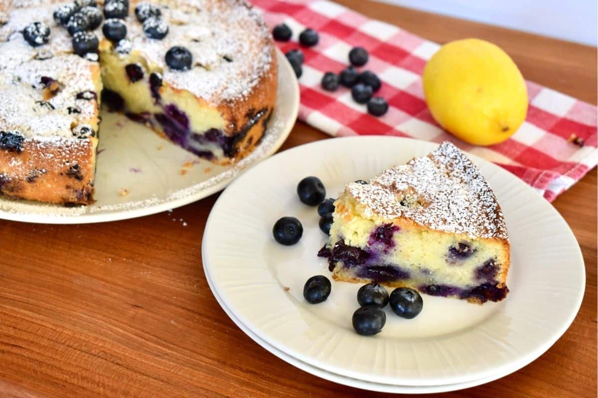 Blueberry Ricotta Cake on a plate with a checkered napkin and lemon in the background. 