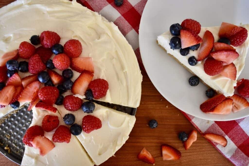 Overhead photo of recipe with berries on to and a slice of cake on a white plate. 