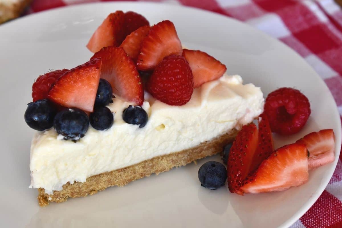 no bake ricotta cheesecake slice on a white plate with fresh berries on top. 