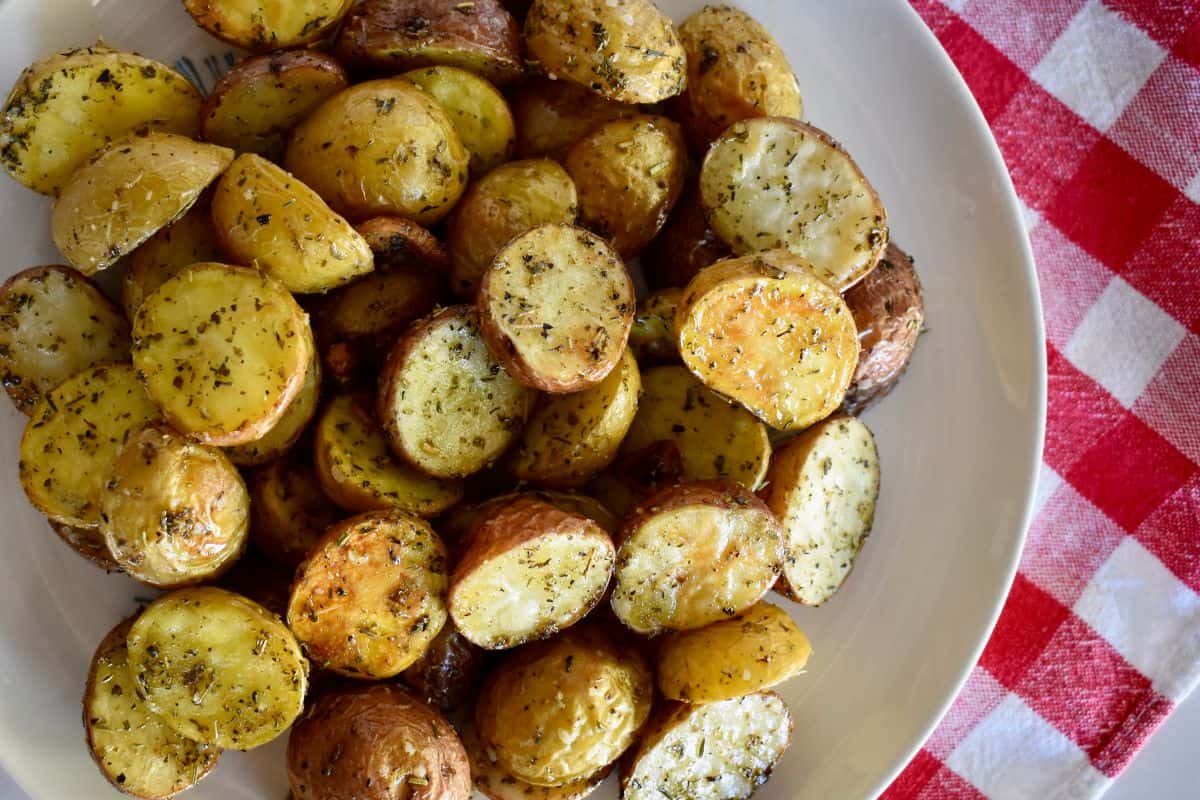 Italian roasted potatoes on a white platter with a checkered napkin underneath. 