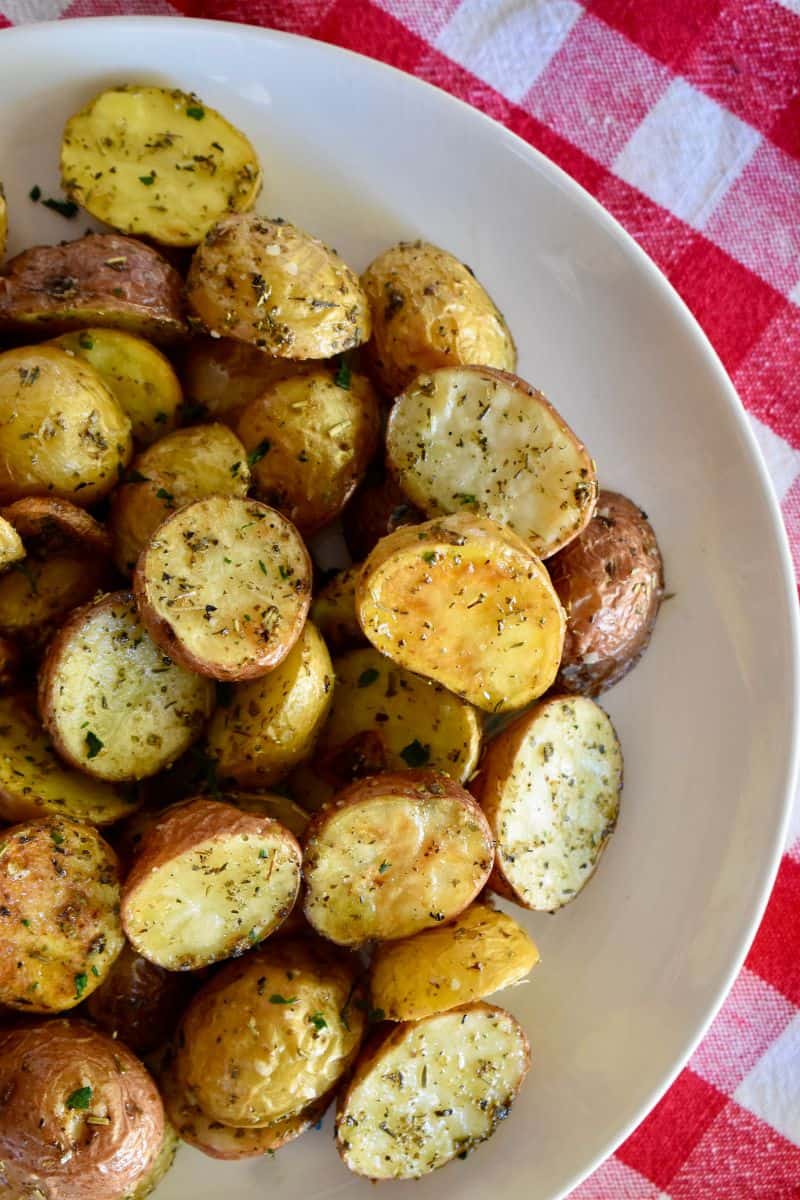 Italian Roasted Potatoes in a white platter on a red and white checkered napkin. 