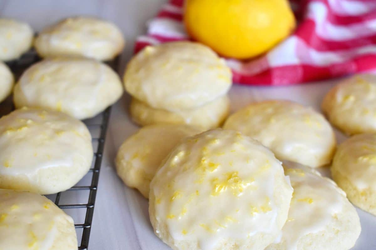 Lemon ricotta cookies on a counter and wire baking rack with a checkered napkin and lemon in the background. 