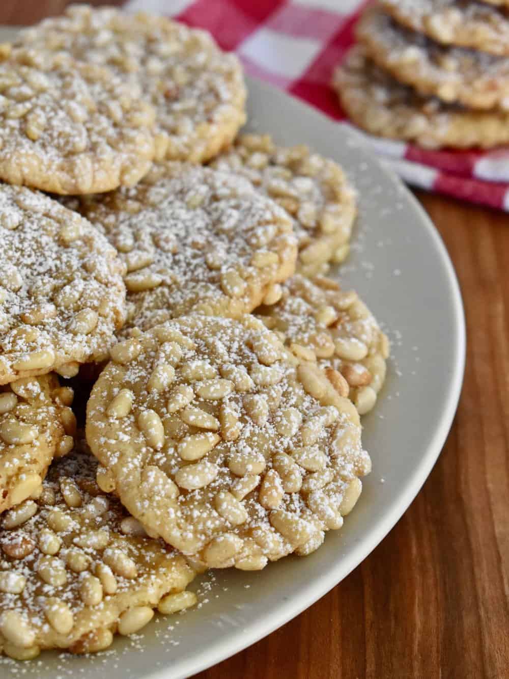 Pignoli Cookies on a plate with powdered sugar sprinkled on them. 